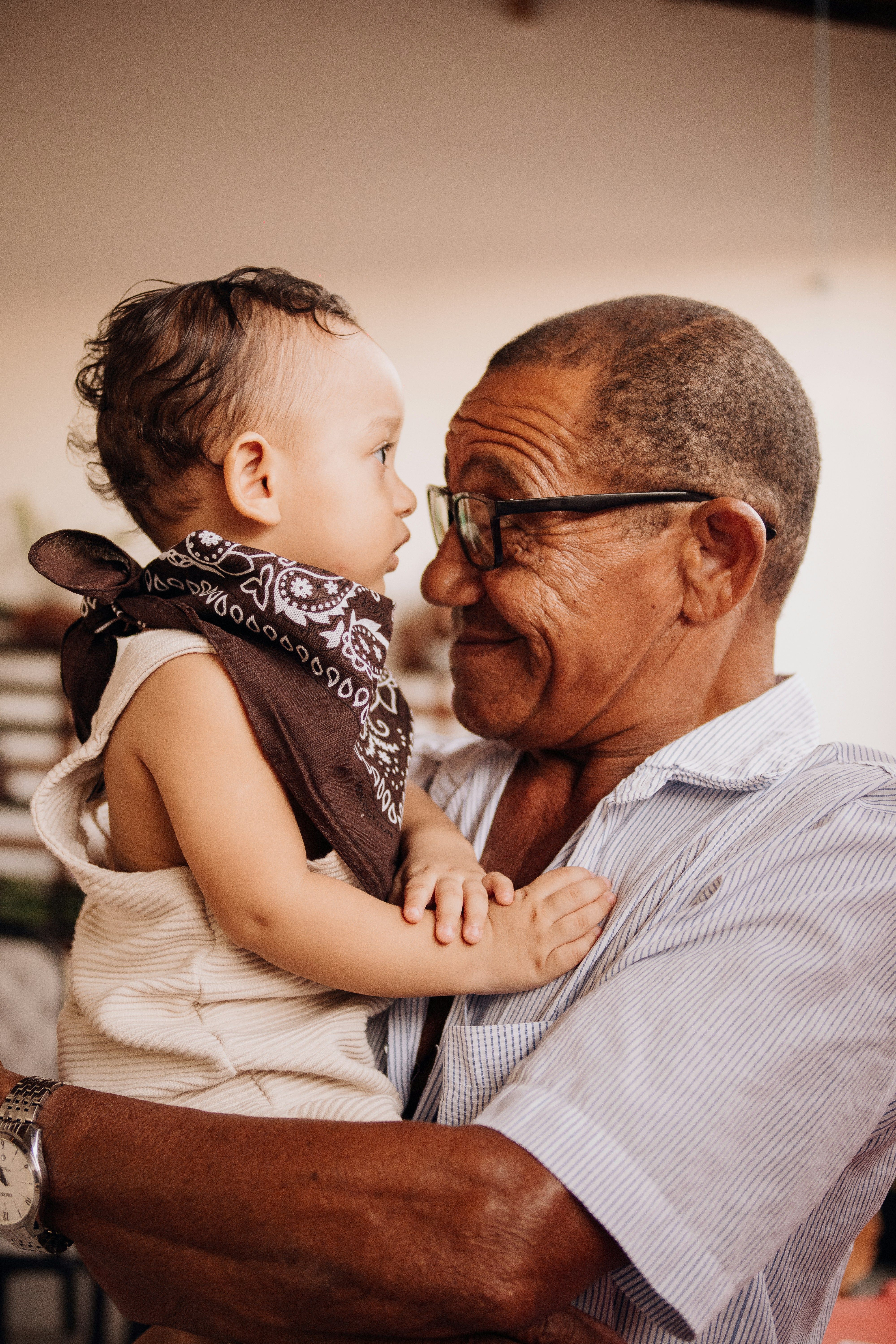 An older man in glasses holds a baby face to face, the two looking at each other.