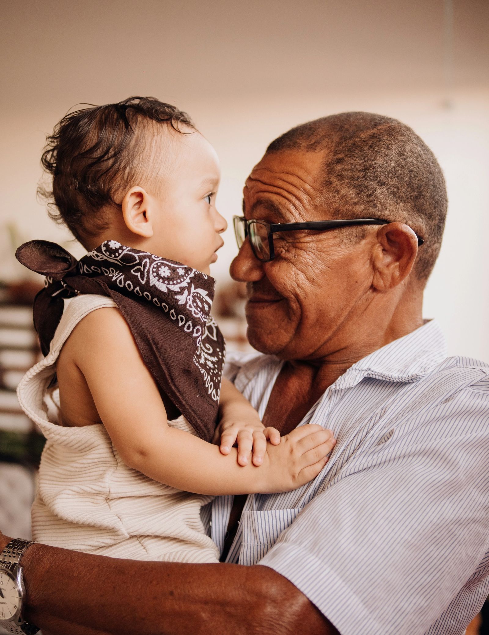 An older man in glasses holds a baby face to face, the two looking at each other.