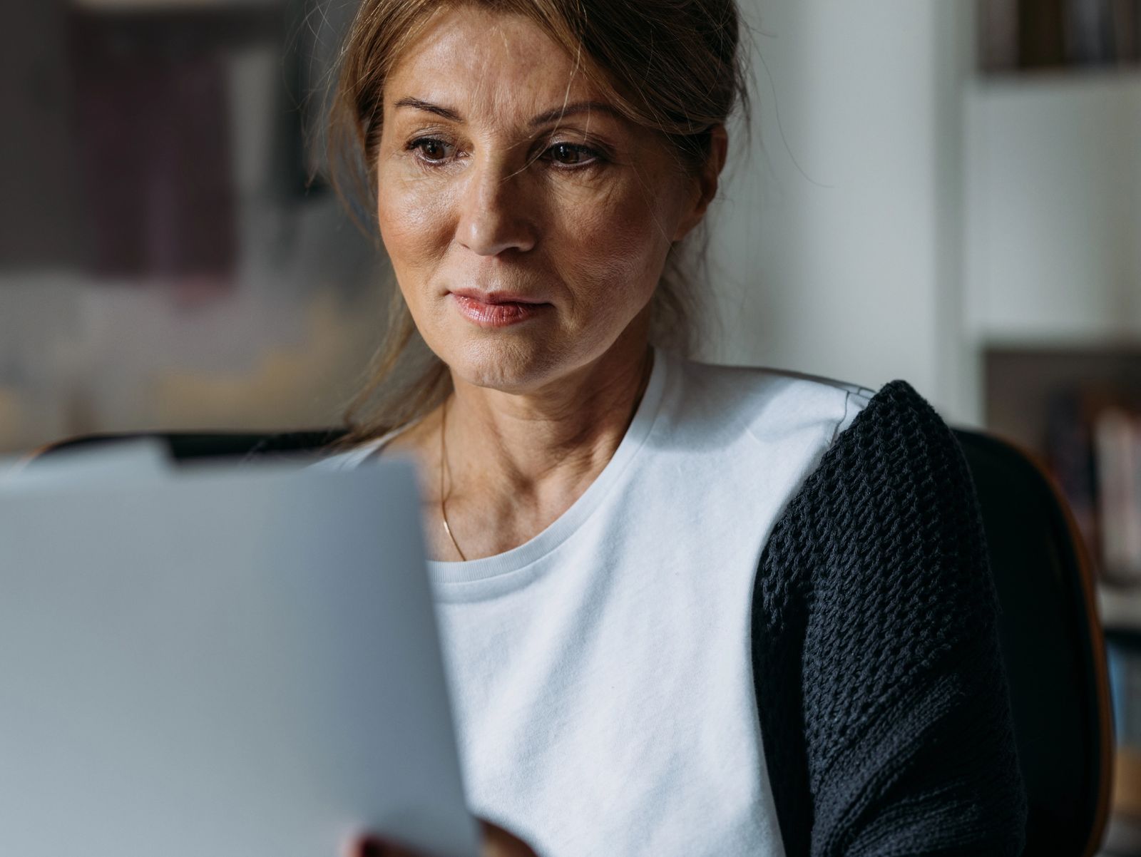 A woman sits in a home office reading a document, bookshelves filling the wall behind her.