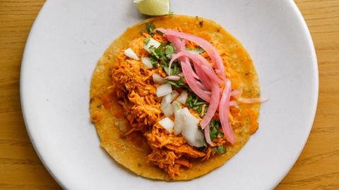 a corn tortilla taco with pulled chicken, diced onion, cilantro, and pickled onion on a white plate