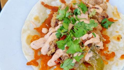 A chicken fajita taco topped with crispy fried cheese, sautéed peppers and onions, creamy fajita sauce, and fresh cilantro, served with a lime wedge on the side.
