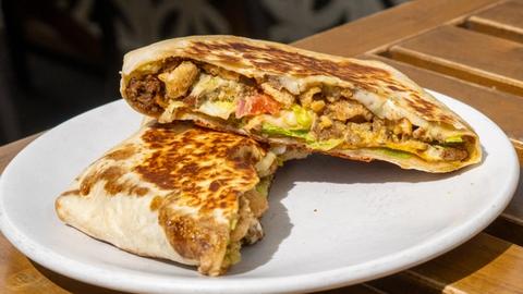 a grilled flour tortilla filled with ground beef, bacon, chicharrónes, and toppings sitting on the sunny patio of Marlo Tacos in Edmonton