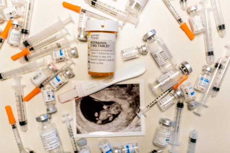 A flat lay of fertility treatment supplies, syringes and medication vials, a positive pregnancy test, and an ultrasound photo.