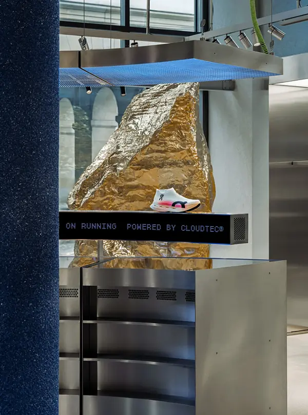 Wide shot of an ON shoe on the interactive display with a gold rock formation installation behind it
