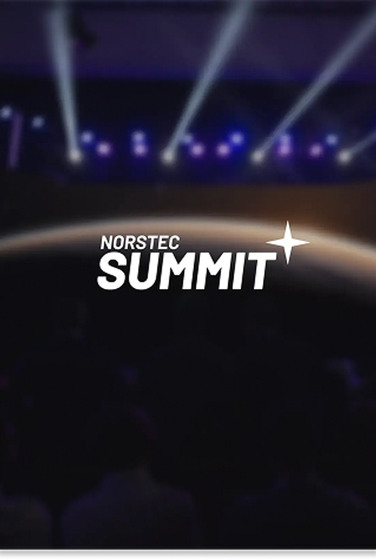 Audience watching a large stage with a screen showing the NORSTEC logo over a planet backdrop, with purple and blue stage lights overhead.