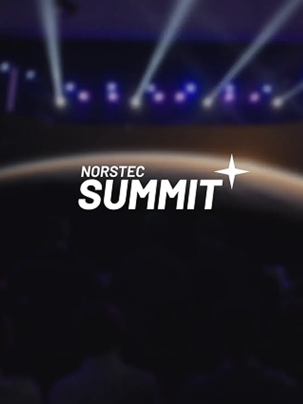 Audience watching a large stage with a screen showing the NORSTEC logo over a planet backdrop, with purple and blue stage lights overhead.