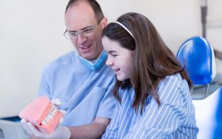 Image of a dentist holding a 3D model of a set of teeth.