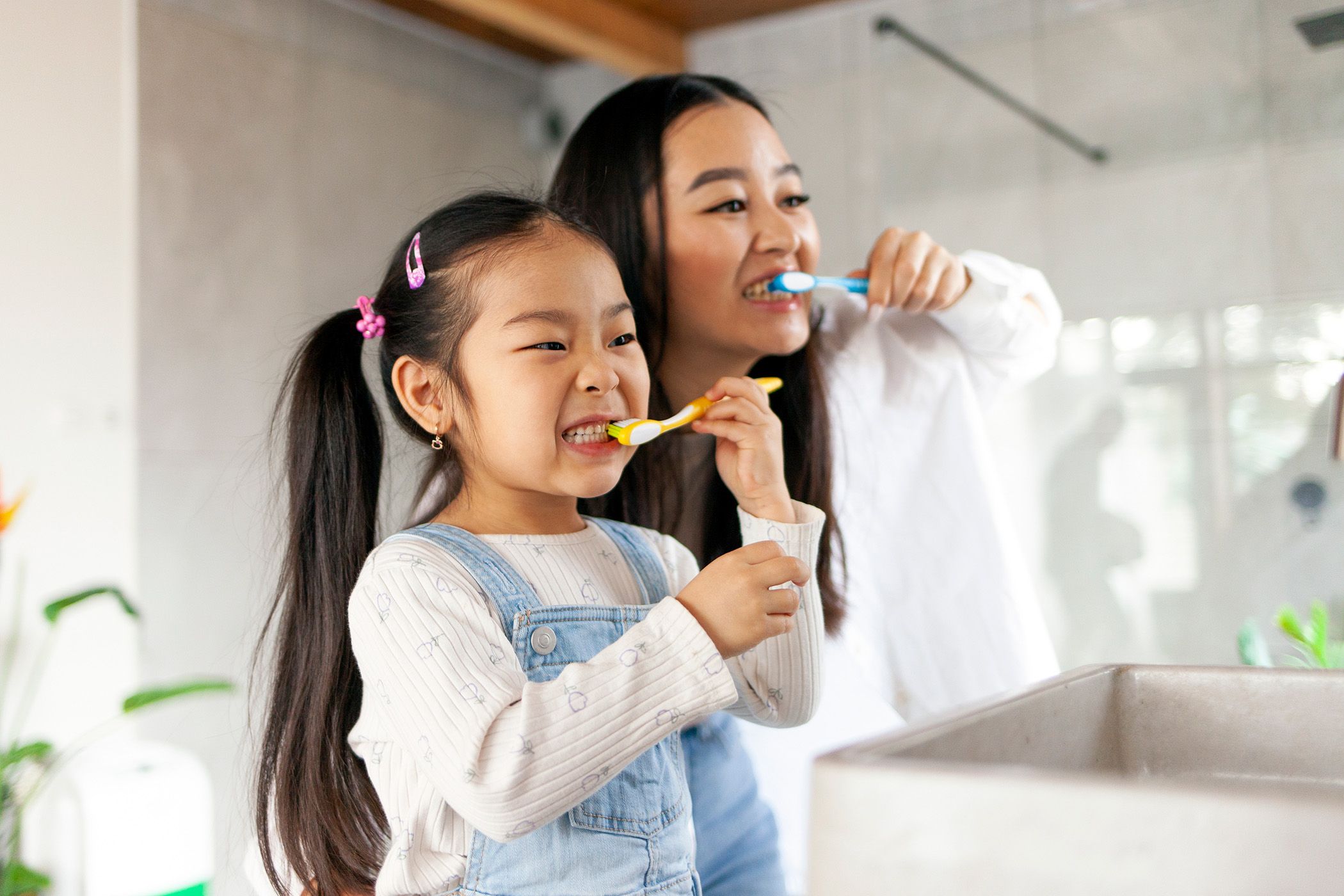 Image of a mother brushing her teeth along side with her daughter.