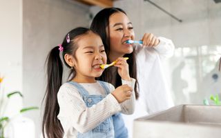 Image of a mother brushing her teeth along side with her daughter.