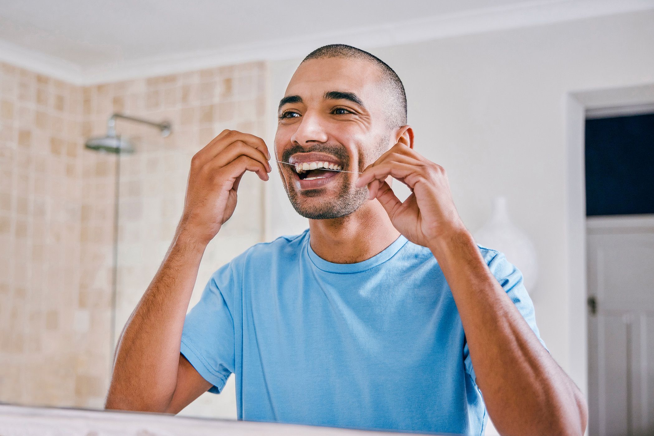 Image of a man at home flossing his teeth.