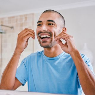 Image of a man at home flossing his teeth.