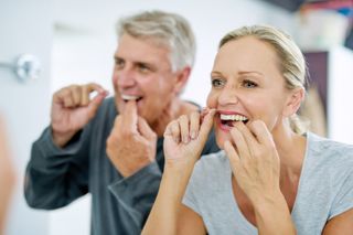Image of an couple flossing their teeth at their home.
