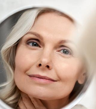 Middle aged woman looking into the mirror - can Invisalign change my face and make me look younger?