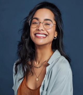 Image of a female with a navy blue background, smiling with her white teeth. Get your white smile at our dental clinic.