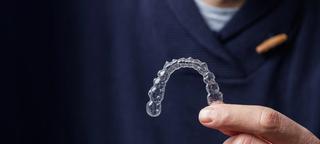 Image of a dentist holding a clear aligner in their hand.