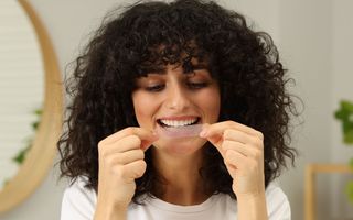 Image of a patient at her home putting on her teeth whitening strips on her teeth.