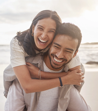 A happy couple on a beach, smiling while one is giving the other a piggyback.
