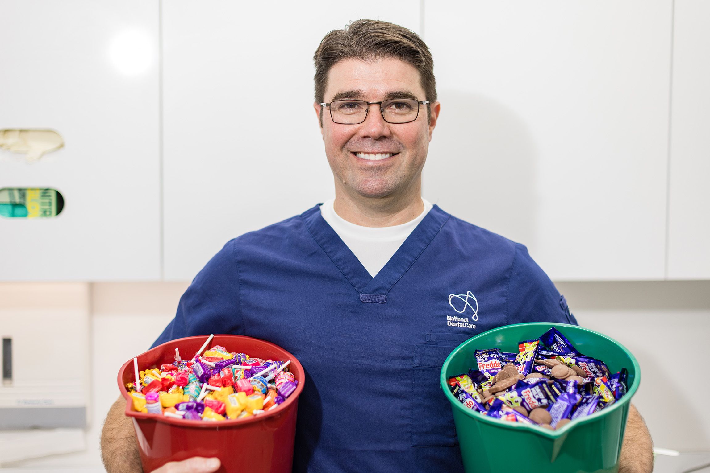 Dr Anthony Benedetto, Lead Dentist at NDC Erina, holding two buckets of chocolate and lollies.