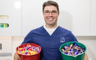 Dr Anthony Benedetto, Lead Dentist at NDC Erina, holding two buckets of chocolate and lollies.