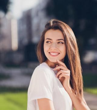 Image of a female with a navy blue background, smiling with her white teeth. Get your white smile at our dental clinic.