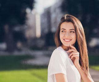 Image of a female with a navy blue background, smiling with her white teeth. Get your white smile at our dental clinic.