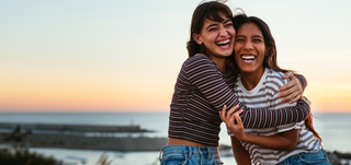 Image of a young female couple in the coast showing their beeming white teeth.