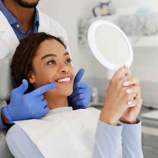 A young female patient holding a mirror, admiring her dental work with her dentist.