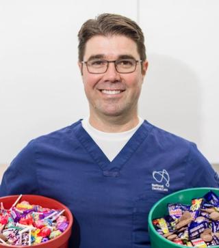 Dr Anthony Benedetto, Lead Dentist at NDC Erina, holding two buckets of chocolate and lollies.