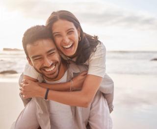 Image of a young couple on the beach smiling with each other.