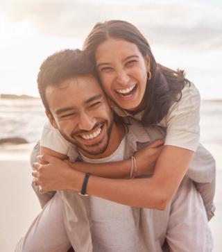 Image of a young couple on the beach smiling with each other.
