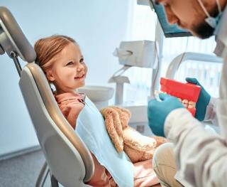 Image of a child being taught how to brush their teeth by her parent and dentist by her side.
