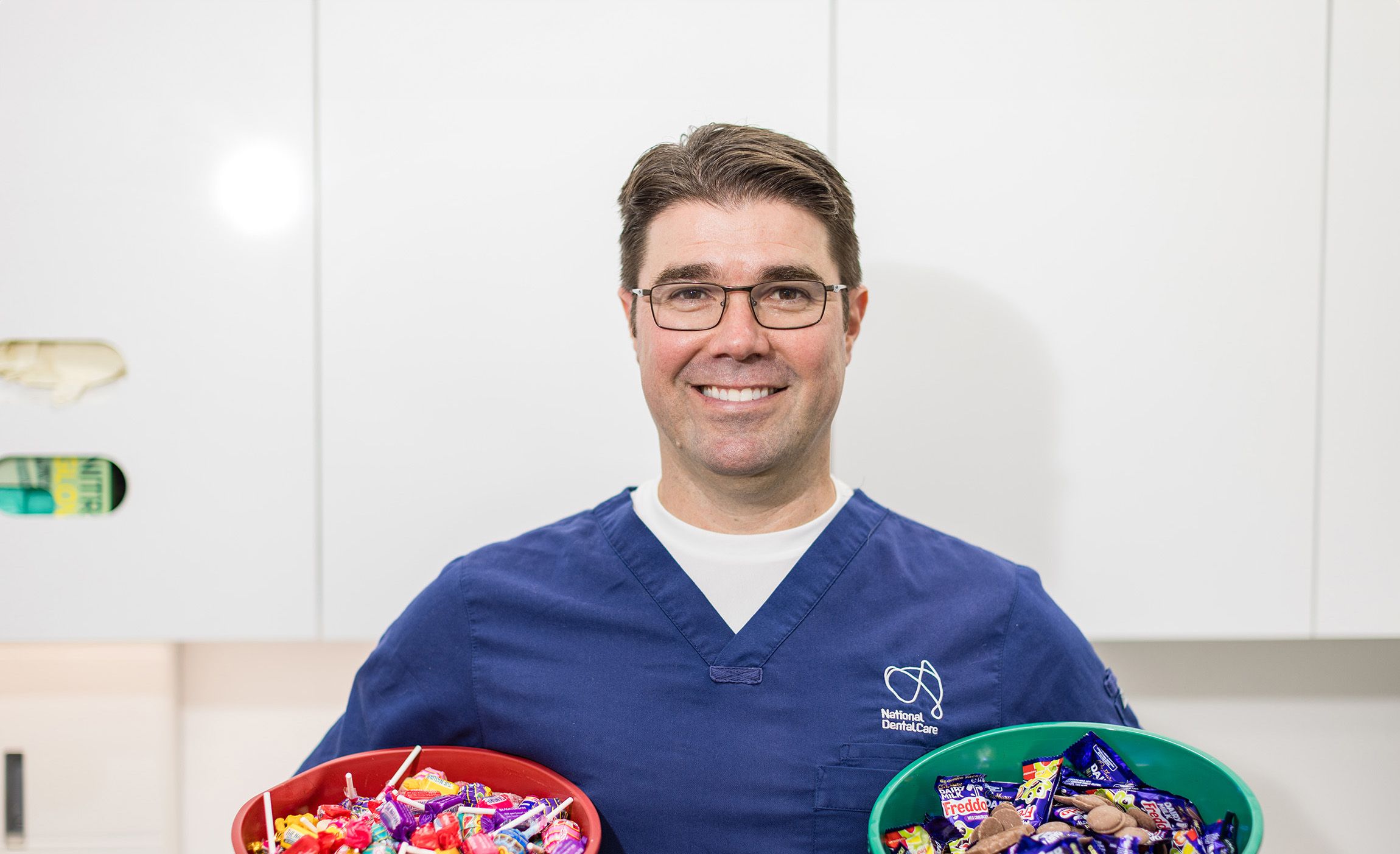 Dr Anthony Benedetto, Lead Dentist at NDC Erina, holding two buckets of chocolate and lollies.