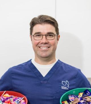 Dr Anthony Benedetto, Lead Dentist at NDC Erina, holding two buckets of chocolate and lollies.