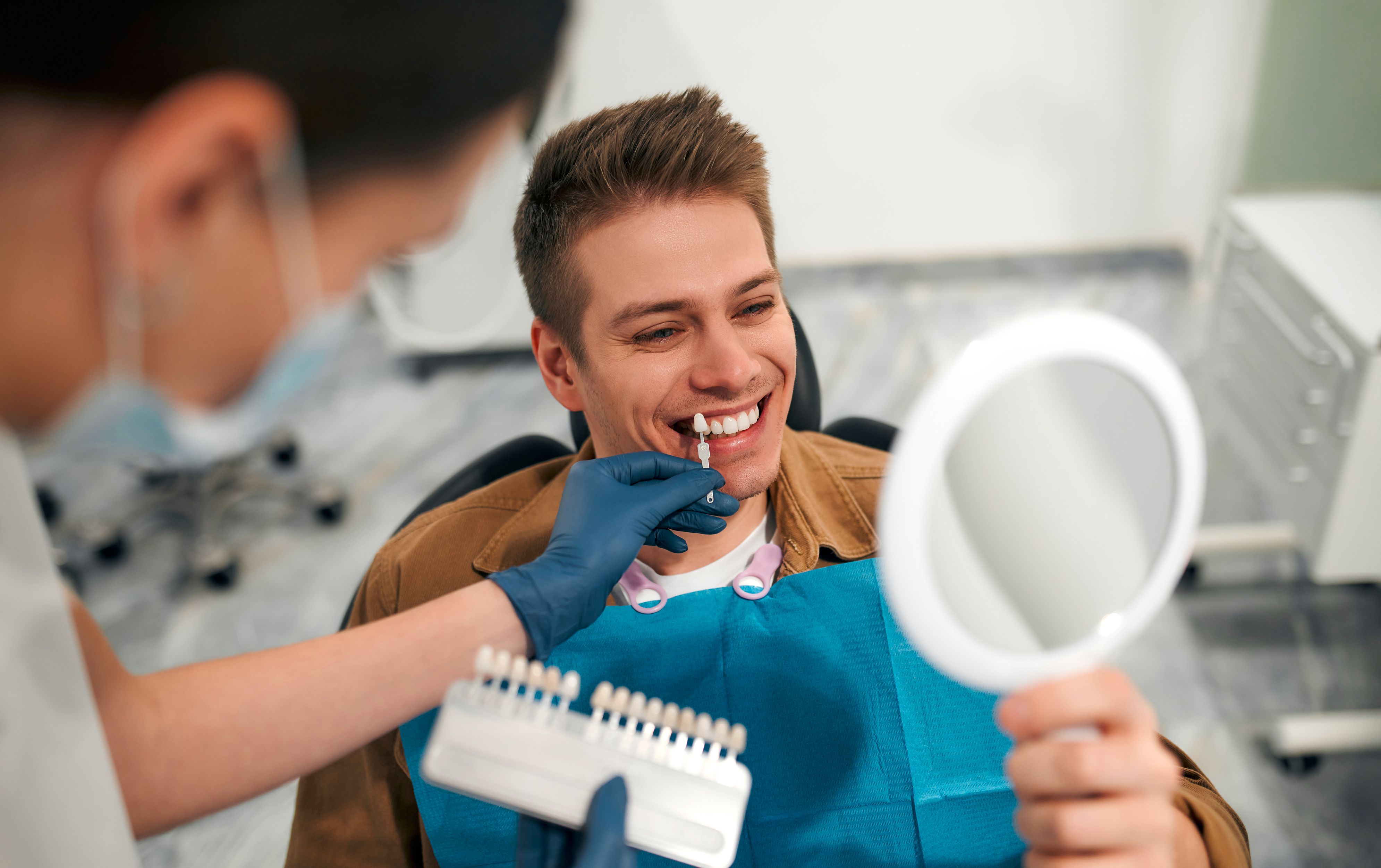 Happy male patient with dentist seeing the colour of his teeth