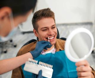 Happy male patient with dentist seeing the colour of his teeth