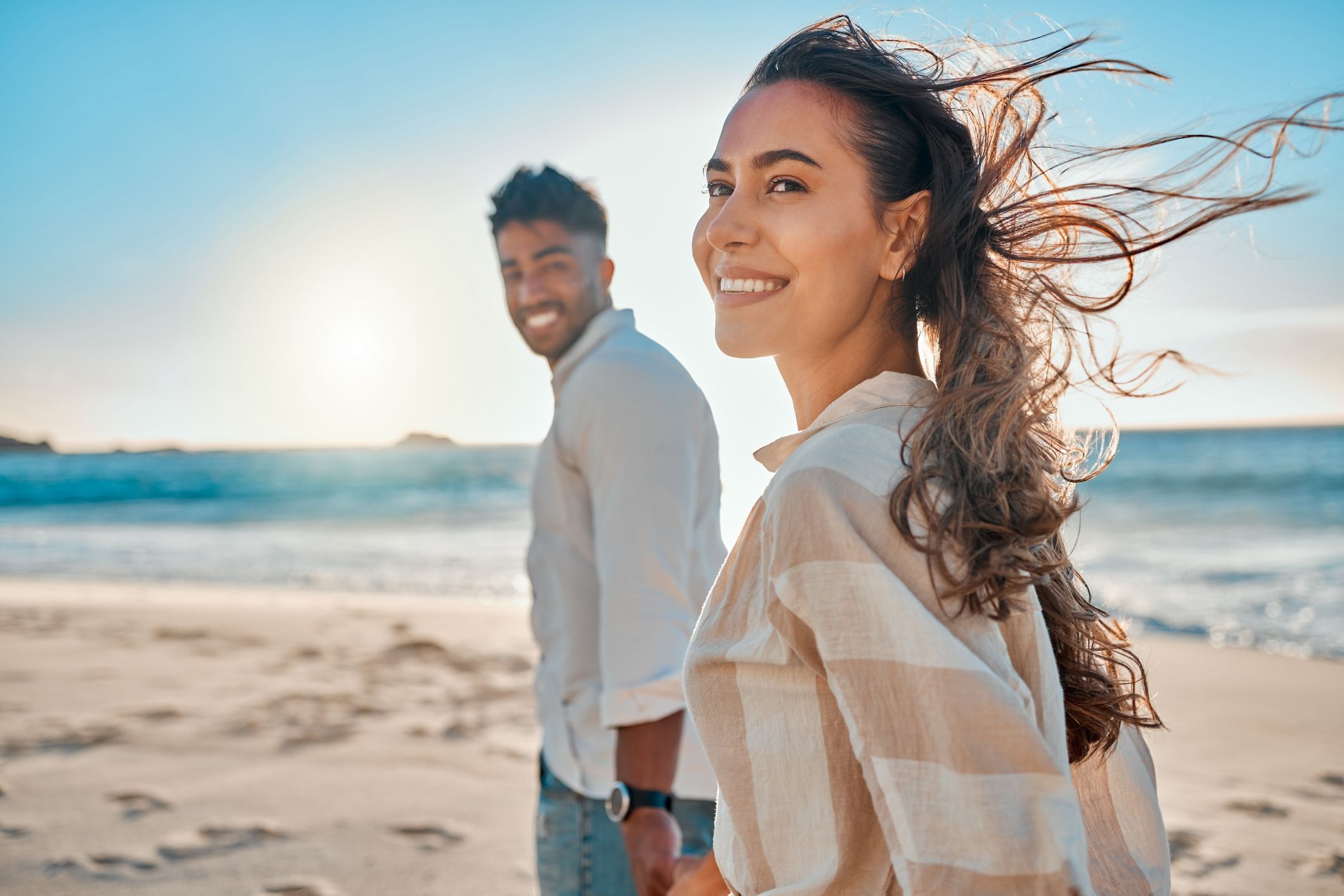 An image of a happy couple on a beach with their whitened teeth
