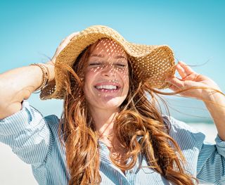 Image of woman smiling in the sun holding onto her hat.