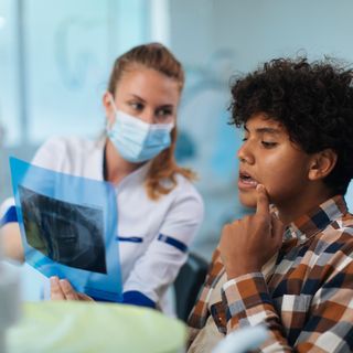 Image of a teenager in a dental chair with his dentist, going over their x-ray results.