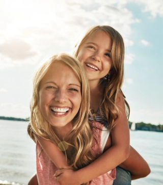 Image of a female with a child on her shoulder smiling, welcome to National Dental Care Box Hill.