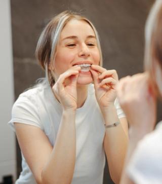 Image of an young woman in her bathroom putting on her clear aligners.