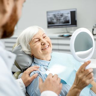 Image of an elderly patient inspecting her new dentures with her dentist.