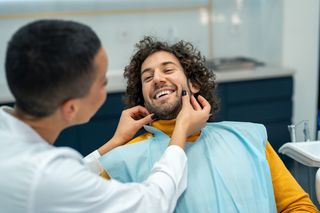 Image of a dentist with her patient making him smile on the dental chair.