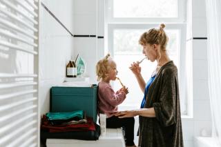Image of a mother brushing her teeth with her daughter at her bathroom.