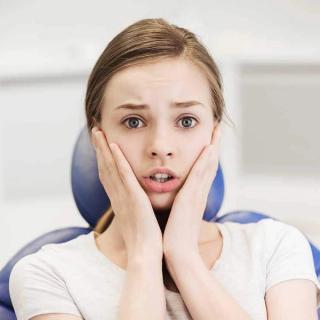 Image of a female patient in a dental chair holding her face in pain.