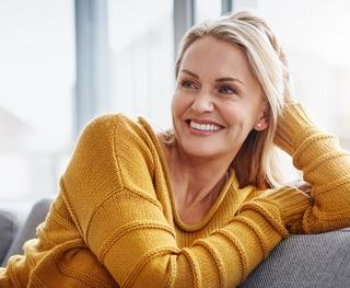 A woman wearing a yellow jumper smiling while sitting on a couch