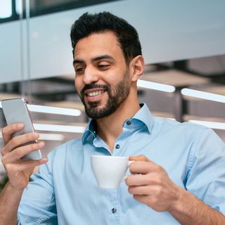 Image of a man drinking his coffee, taking his time looking at his phone.