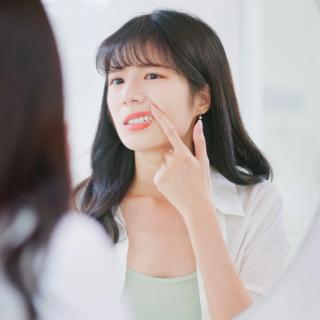 Image of a woman at her home looking at the mirror, she is inspecting her teeth.