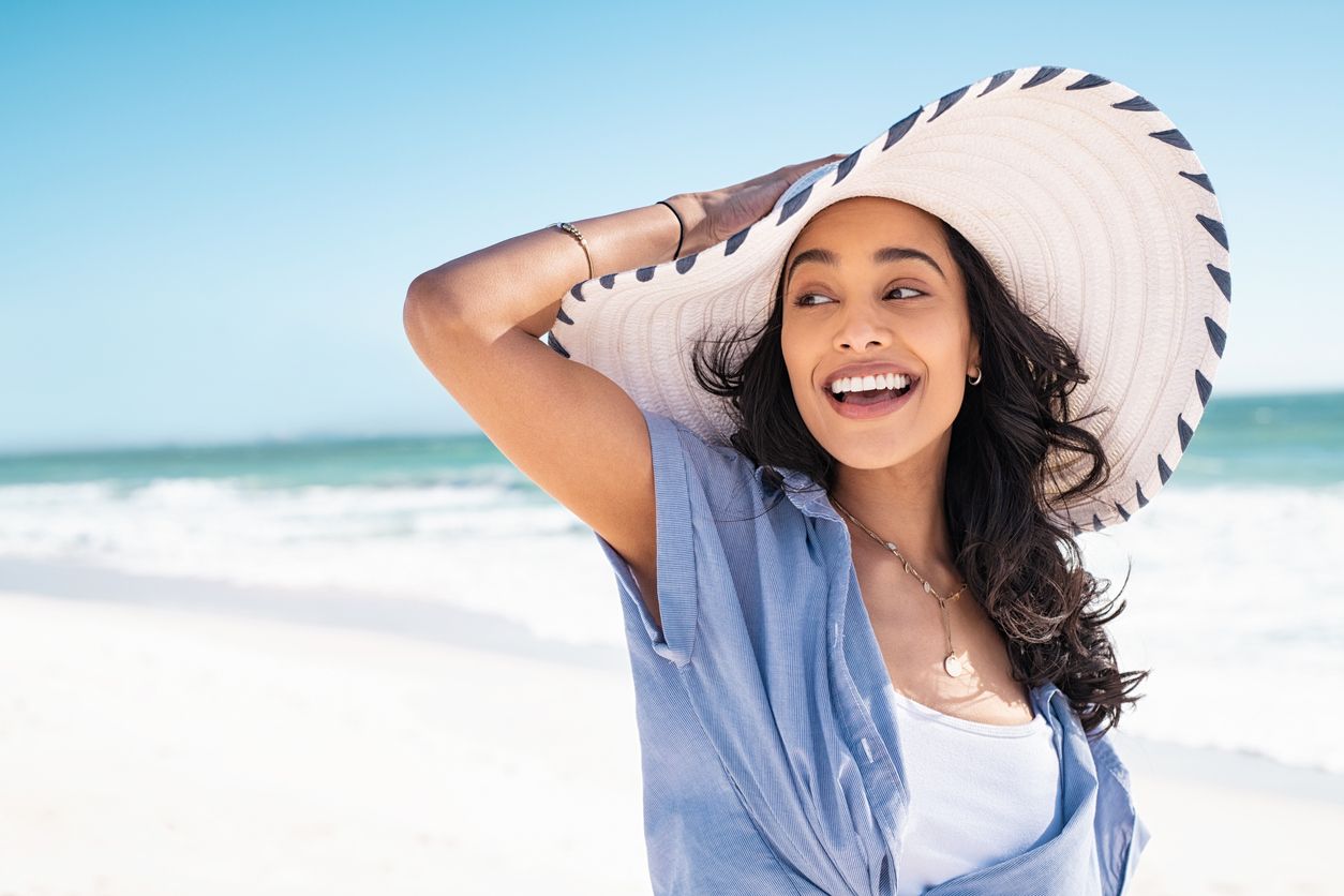 Stock image of female enjoying the beach with a hat and a big smile.
