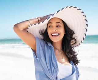 Stock image of female enjoying the beach with a hat and a big smile.