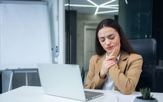 Image of a female in a corporate environment suffering a tooth pain by holding her jaw.